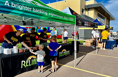 Augustana college students handing out root beer floats to kids under a Reliabank tent at a sponsored event in Sioux Falls.