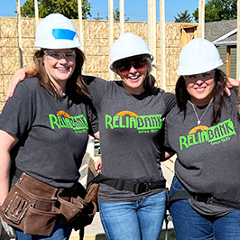 Three Reliabank employees stand together smiling while volunteering on a tiny home building job site for Veterans Community Project.