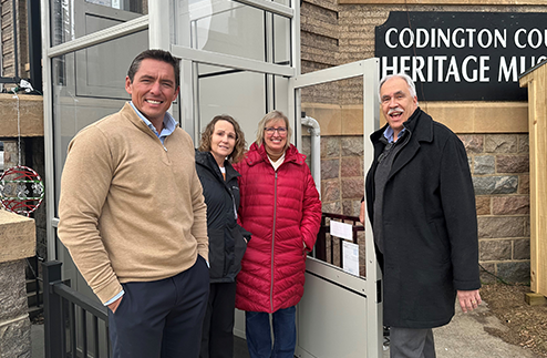 Three Reliabank employees stand in the opening of a newly installed elevator at the Codington County Heritage Museum with the director of the museum in Watertown.