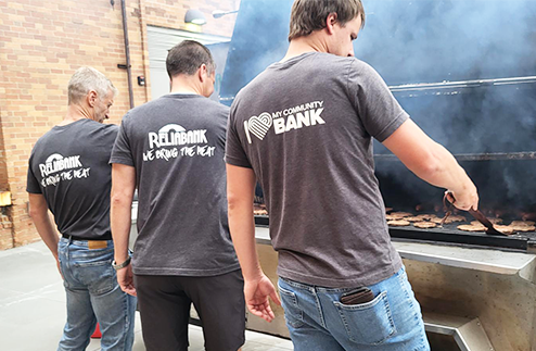 Three Reliabank employees working together at a grill for a fundraiser event serving lunch to teachers in Watertown.